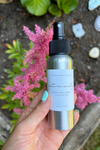 Hand holding a silver spray bottle with a label against a natural background