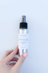 A hand holding a silver spray bottle labeled 'intentionality' with a spray nozzle on top.